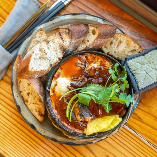 Vietnamese baked eggs with tomato sauce, mushrooms, and cilantro, served with toasted baguette slices.