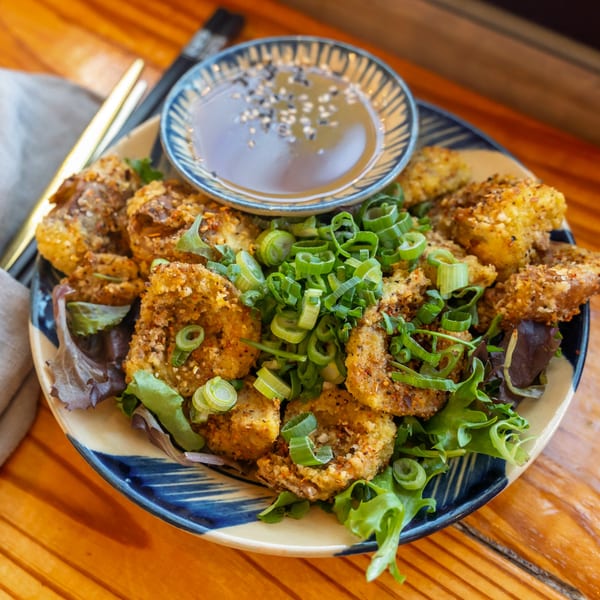 Crispy Vietnamese fried tofu with green onions and a side of dipping sauce on a wooden table.