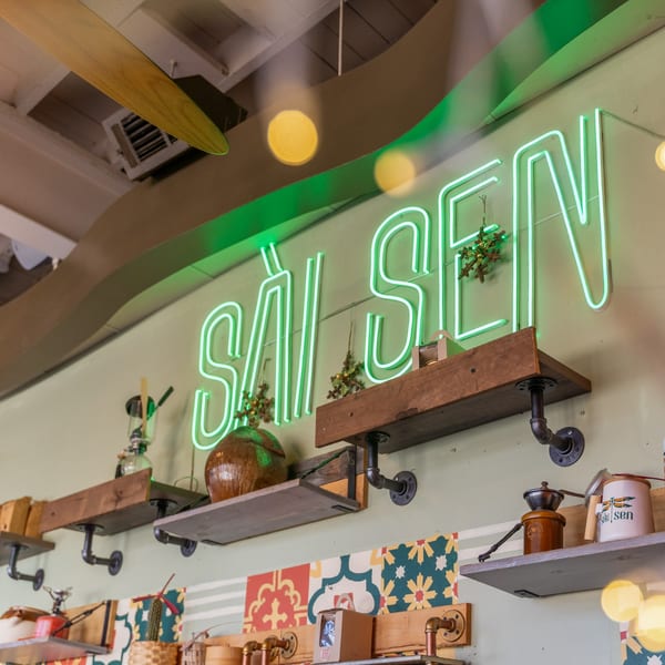Green neon "SAI SEN" sign above shelves with decorative items and colorful patterned tiles.