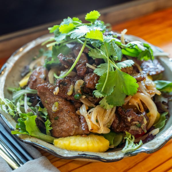 Vietnamese shaking beef salad with greens, onions, and cilantro, served in a decorative bowl.