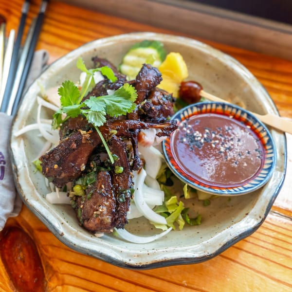 Vietnamese grilled quail with cilantro, onions, and dipping sauce on a rustic plate.