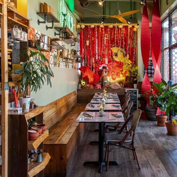 Interior of Sen Organic Small Plate, a Vietnamese restaurant, with festive red and gold decor, wooden benches, and marble tables.