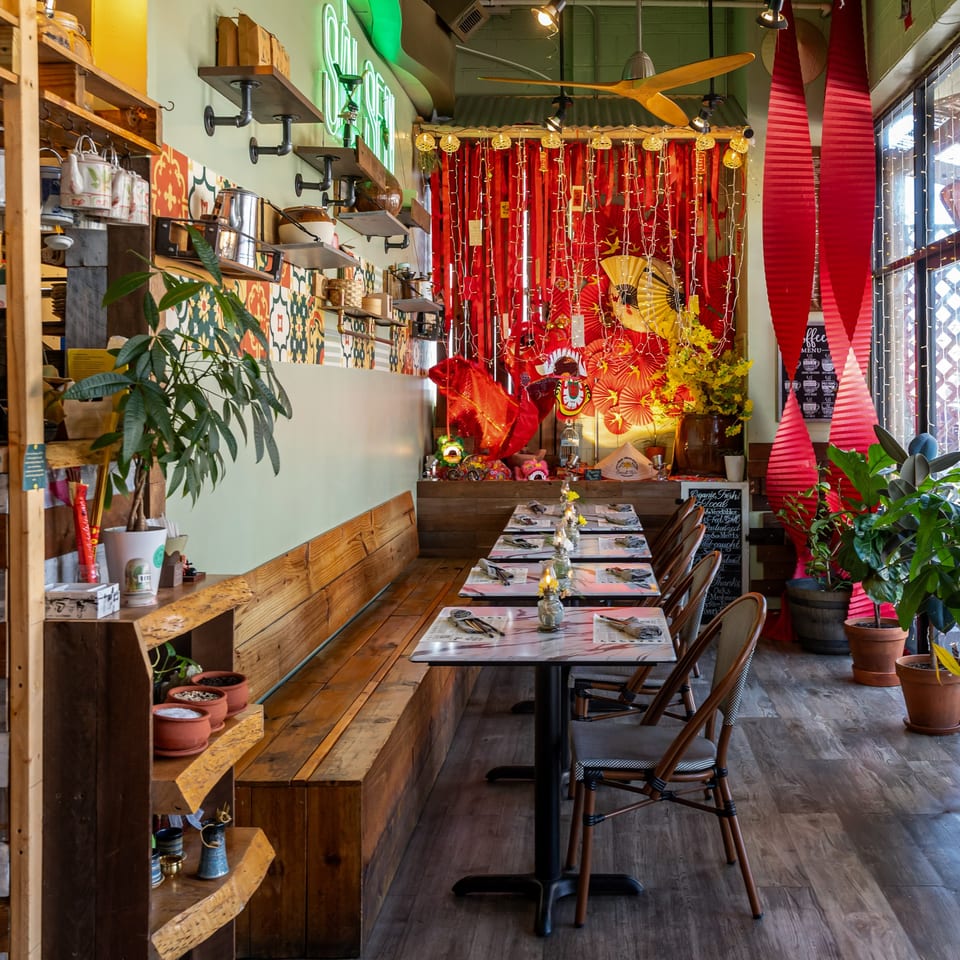 Interior of Sen Organic Small Plate, a Vietnamese restaurant, with festive red and gold decor, wooden benches, and marble tables.